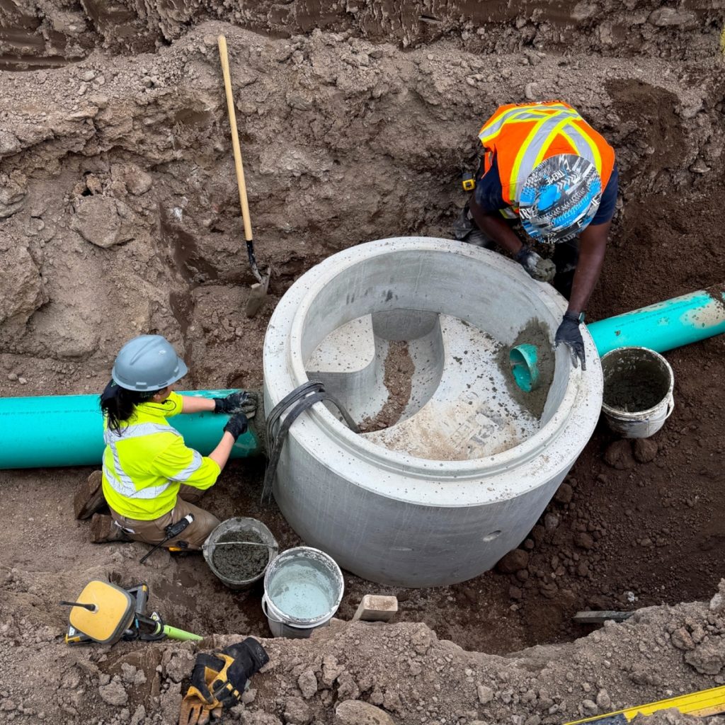 Dawson Civil crew members installing a precast concrete storm manhole connected to storm main piping during municipal infrastructure construction in Fraser Lake, British Columbia.