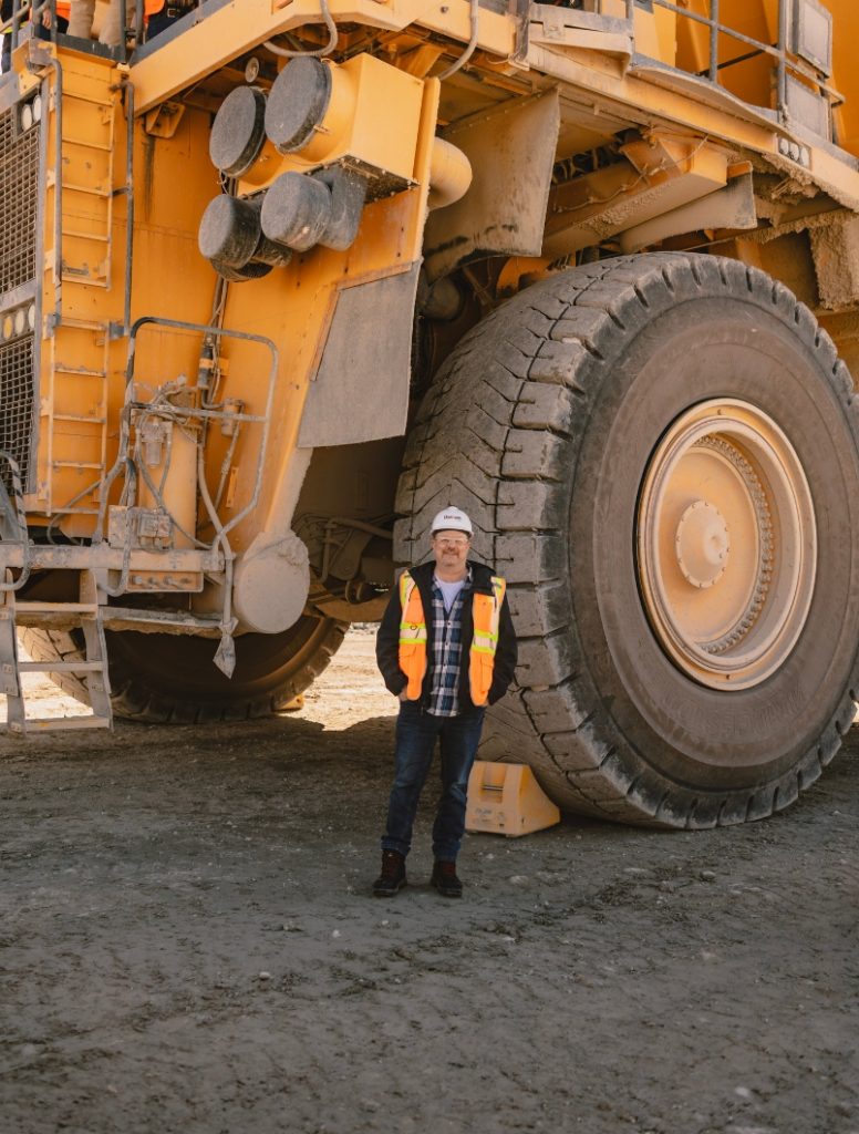 Shane Gowans standing beside a large haul truck tire at Gibraltar Mine in British Columbia.